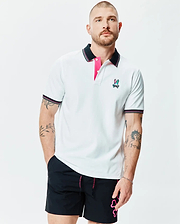 Mens Nate Pique Polo, a white classic fit pique polo with black collar and cuffs featuring pink and white tipping, hot pink placket lining, and a small embroidered multi-color Psycho Bunny skull logo on the left chest.