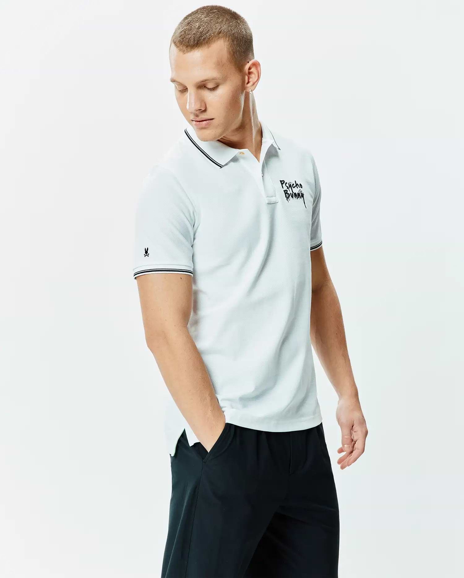 Mens Duncan Pique Polo, a light blue classic fit pique polo with black and white striped collar/cuffs, featuring a large black Psycho Bunny script chest logo and small bunny skull sleeve logo.