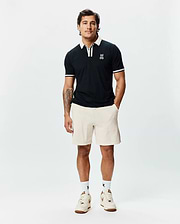 Mens Ridley Pique Polo, a classic fit black pique polo with white tipped collar and sleeve cuffs, featuring a small embroidered Psycho Bunny skull logo on the left chest. (1)