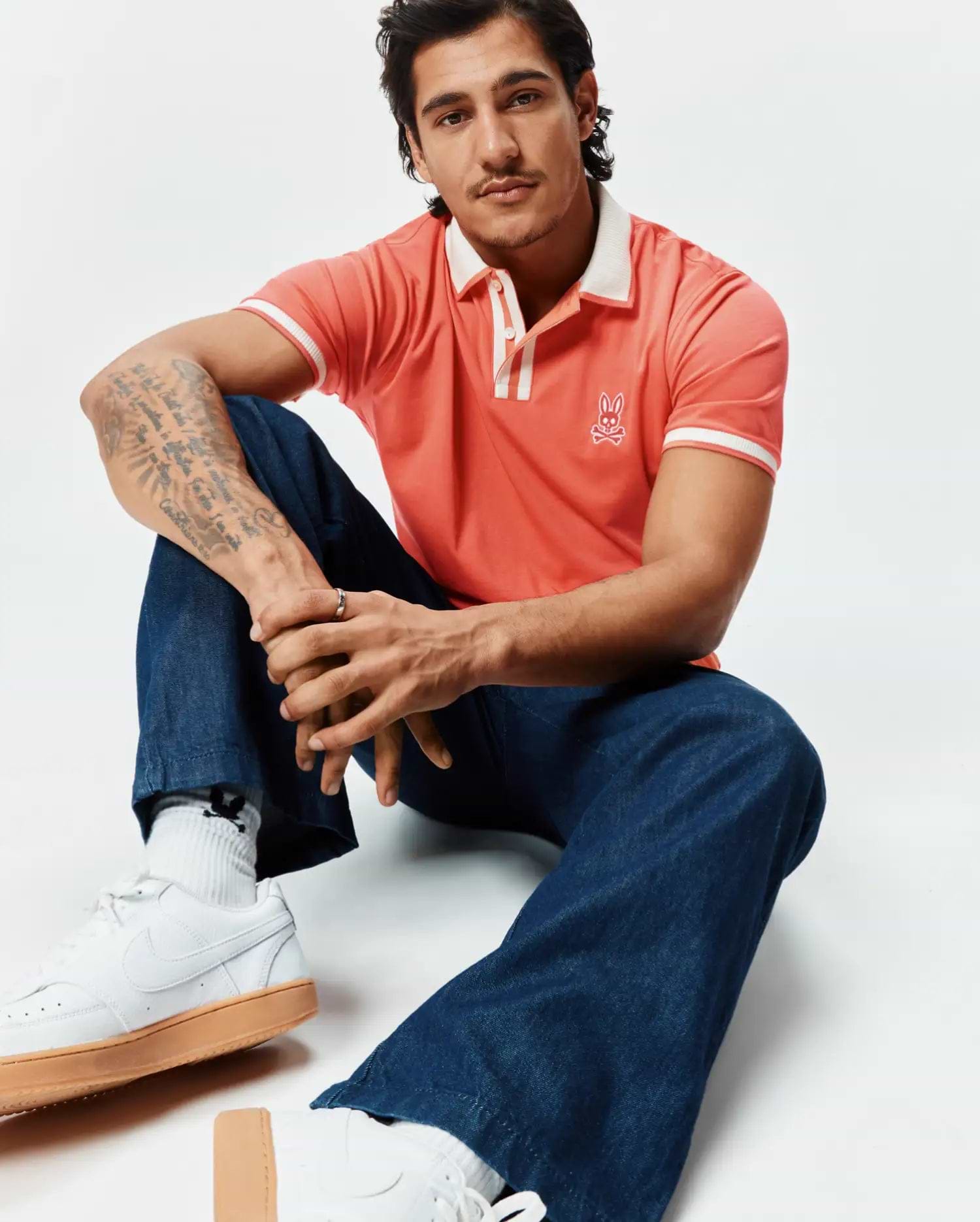 Mens Ridley Pique Polo in vibrant coral pique, classic fit, with a white ribbed collar, two-button placket, and white striped cuffs. Features a white embroidered Psycho Bunny skull logo on the left chest. (4)