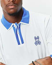 Mens Ridley Pique Polo in white pique, featuring a classic fit, ribbed blue collar, striped blue and white placket, and an embroidered blue Psycho Bunny skull logo on the left chest. (2)