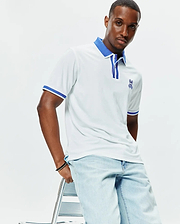 Mens Ridley Pique Polo, white classic fit pique polo with royal blue ribbed collar, striped placket, and cuffs, featuring a medium embroidered royal blue Psycho Bunny skull logo on the left chest. (1)