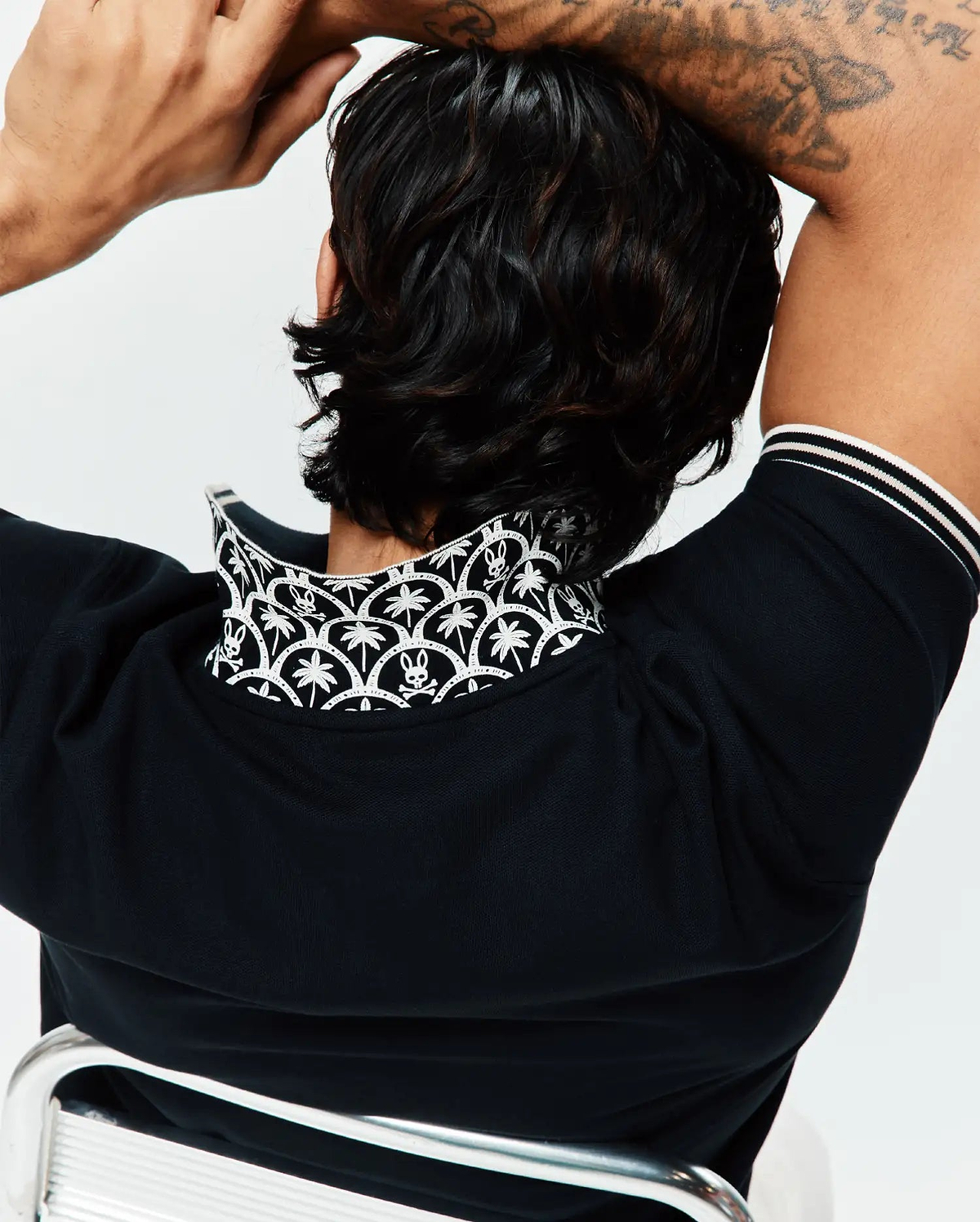 Black Mens Brad Pique Polo, classic pique knit, with a popped collar showcasing a white Psycho Bunny skull and palm tree pattern, plus white striped cuffs. (3)