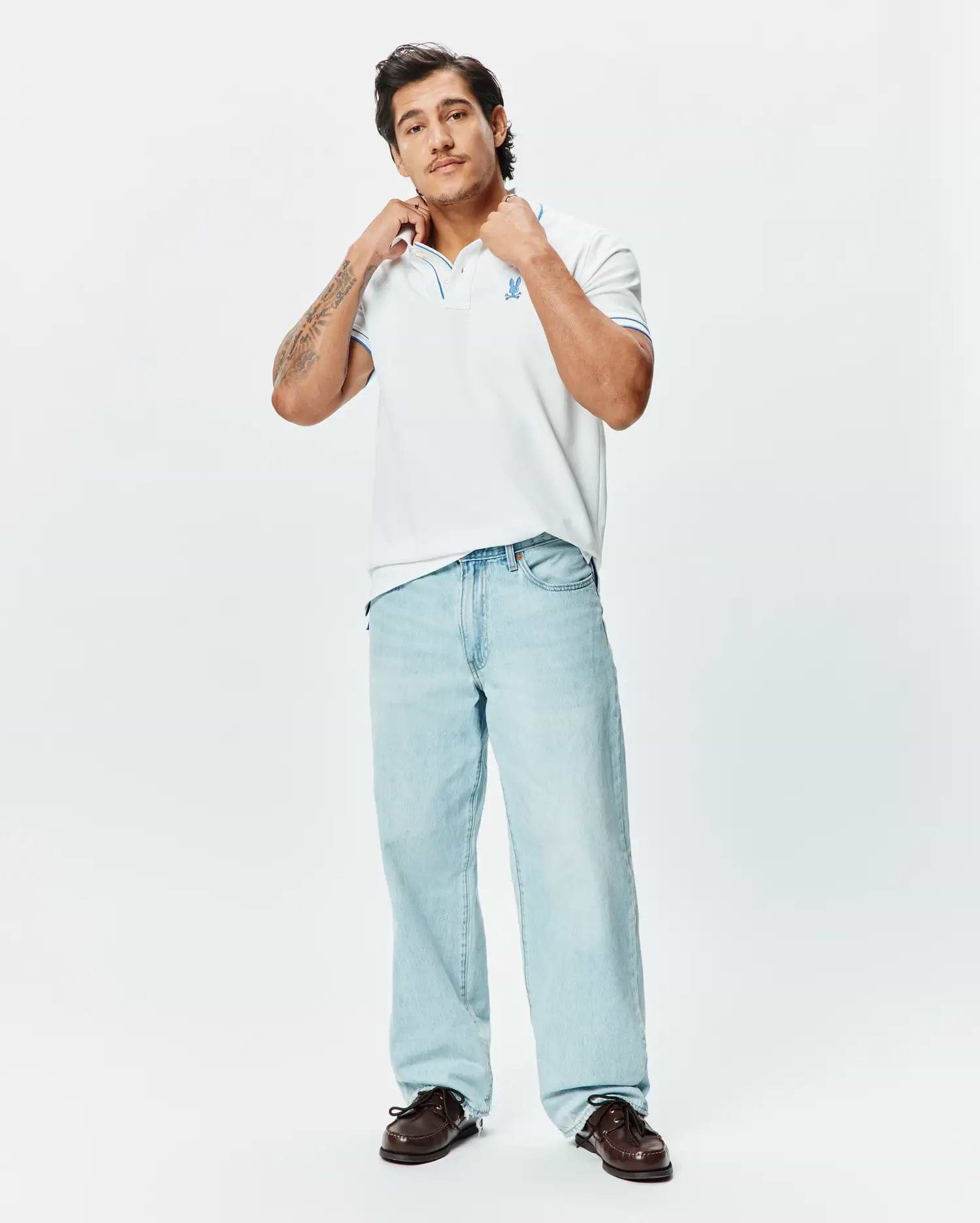 Mens Brad Pique Polo, a classic fit white pique polo with blue tipping on the collar and cuffs, featuring an embroidered blue Psycho Bunny skull logo on the left chest.