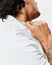 Mens Brad Pique Polo in crisp white, featuring a classic fit, textured pique fabric, and a subtle beige botanical pattern on the inner collar with bright blue piping.