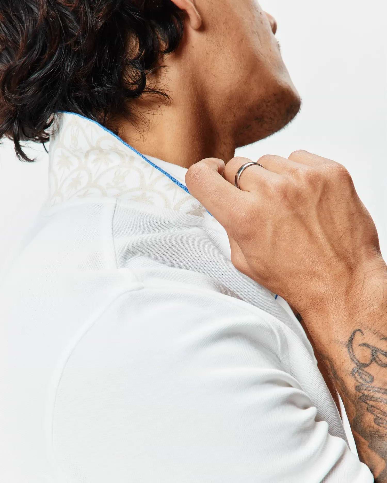 Mens Brad Pique Polo in crisp white, featuring a classic fit, textured pique fabric, and a subtle beige botanical pattern on the inner collar with bright blue piping.