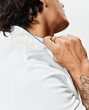 Mens Brad Pique Polo in crisp white, featuring a classic fit, textured pique fabric, and a subtle beige botanical pattern on the inner collar with bright blue piping.