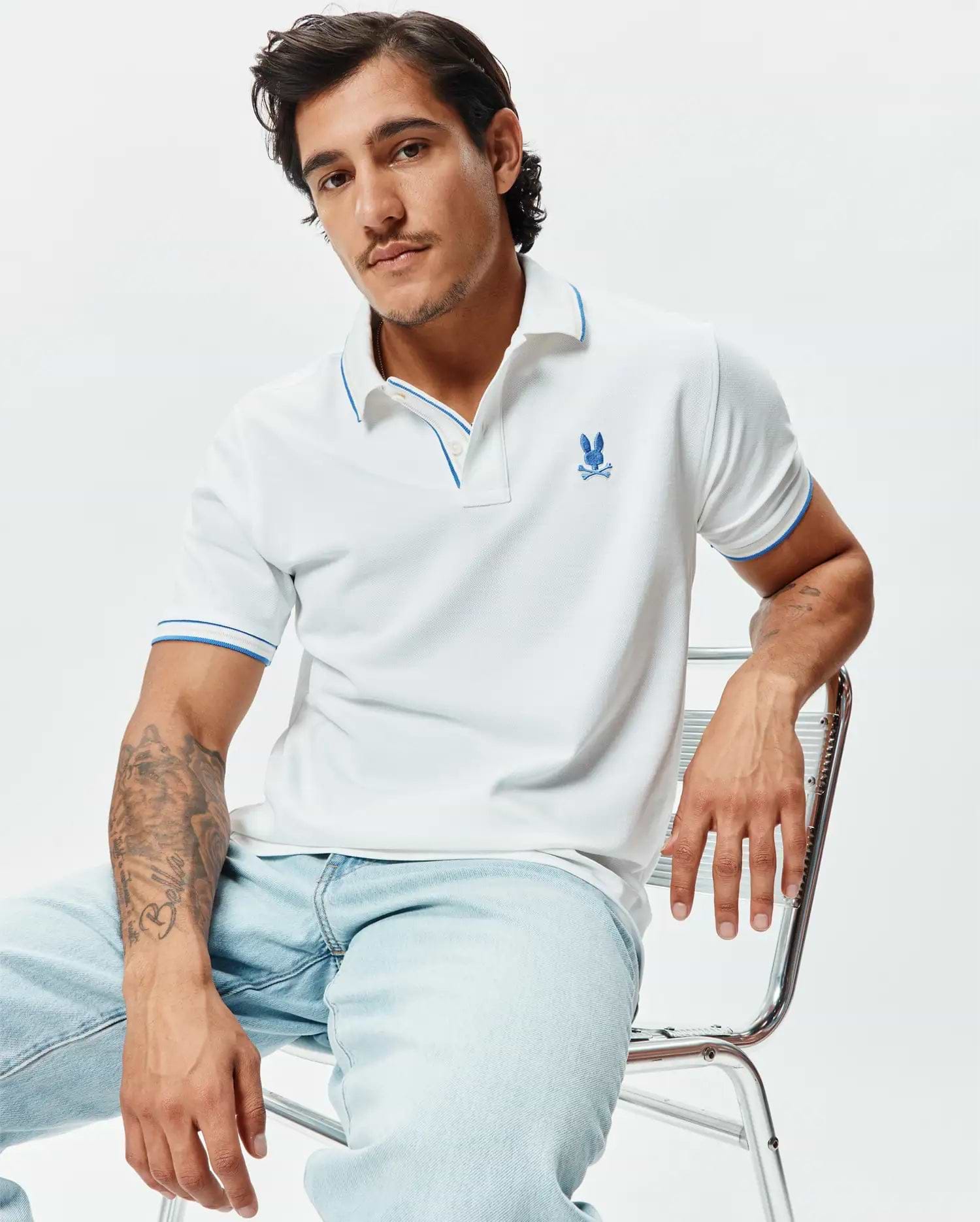Mens Brad Pique Polo, white pique knit with blue trim on collar and sleeve cuffs, featuring an embroidered blue Psycho Bunny skull logo on the left chest, classic fit.