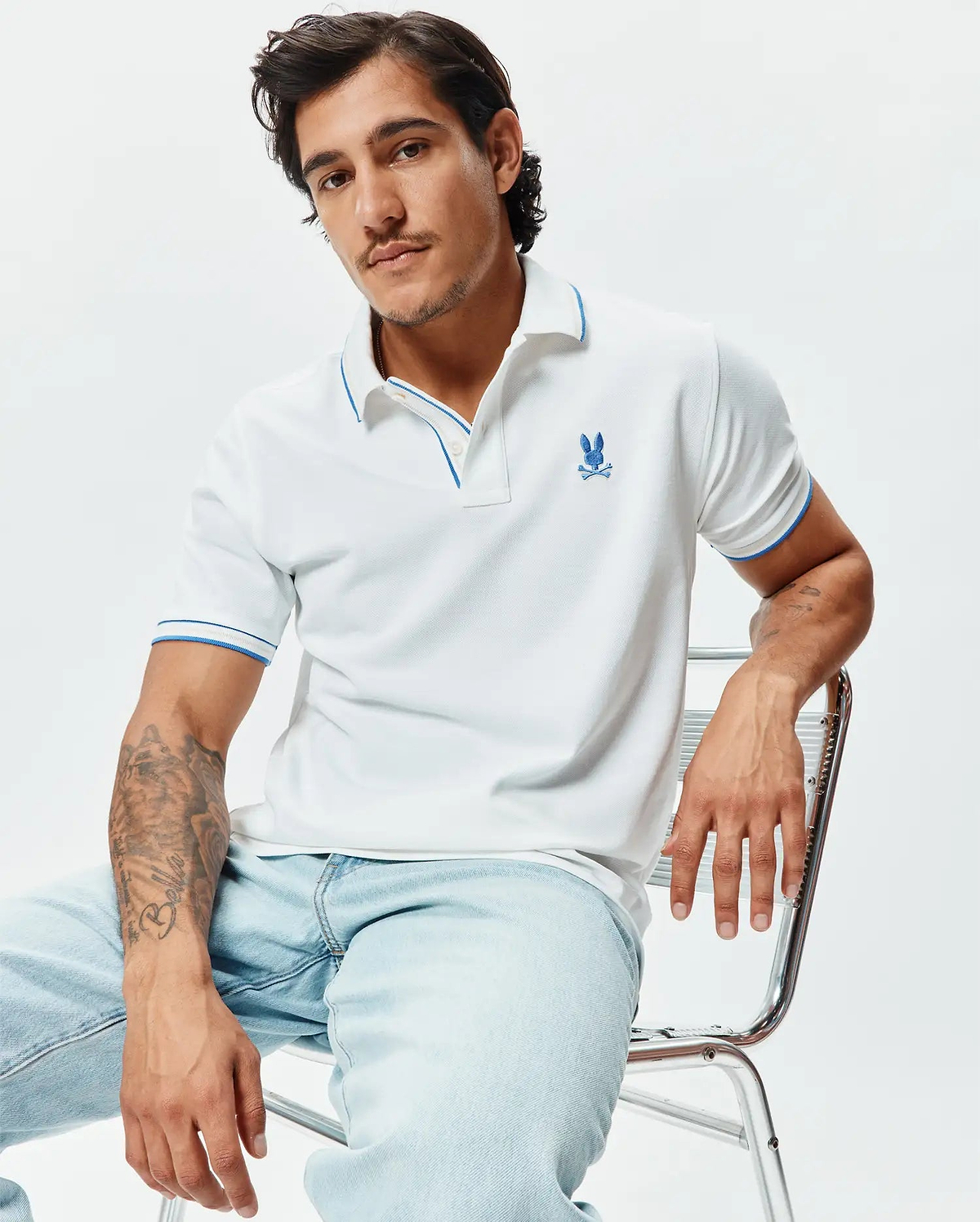 Mens Brad Pique Polo, white pique knit with blue trim on collar and sleeve cuffs, featuring an embroidered blue Psycho Bunny skull logo on the left chest, classic fit.