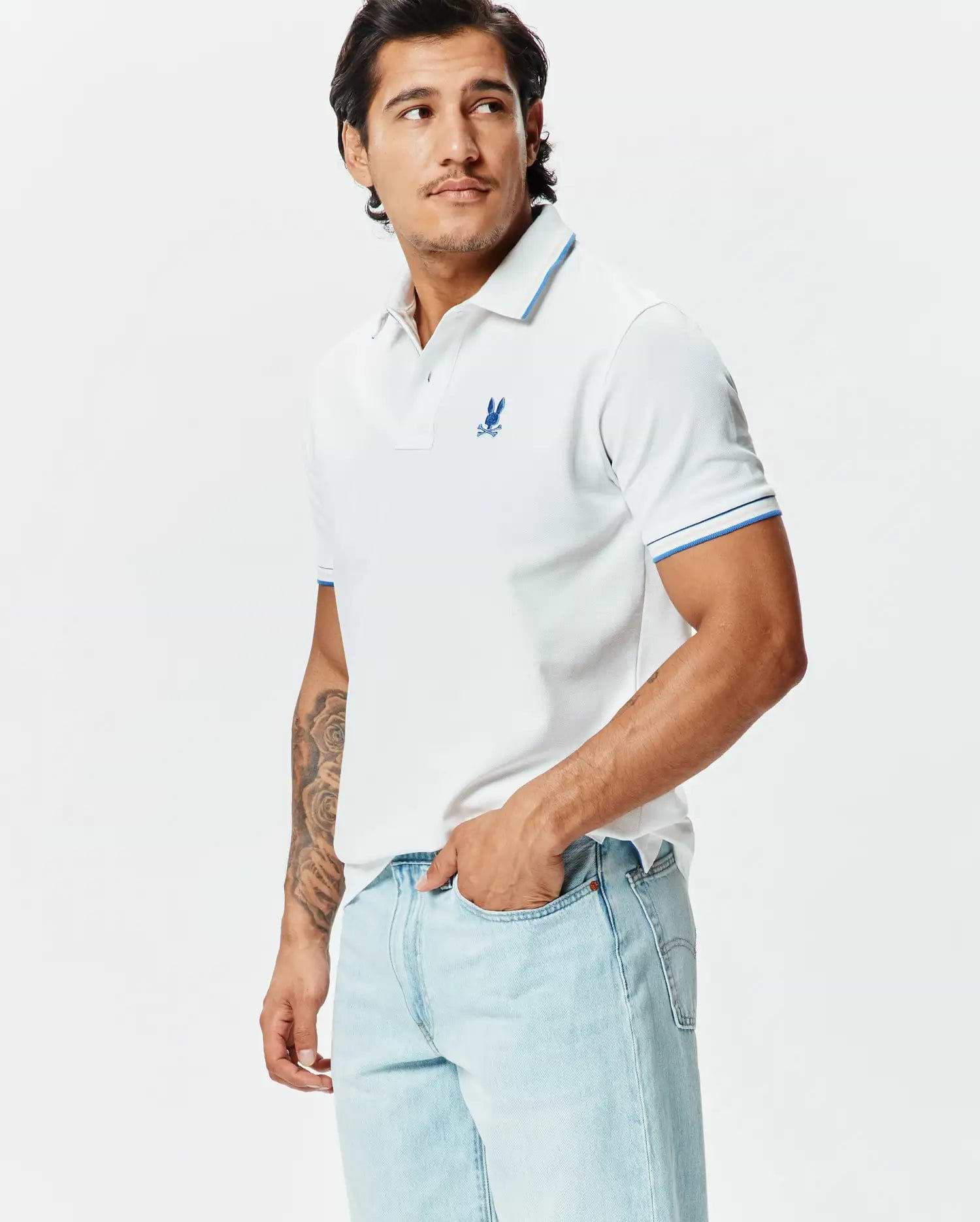 Mens Brad Pique Polo: White classic fit pique polo with blue tipped collar and cuffs, featuring a small embroidered blue Psycho Bunny skull logo on the left chest.