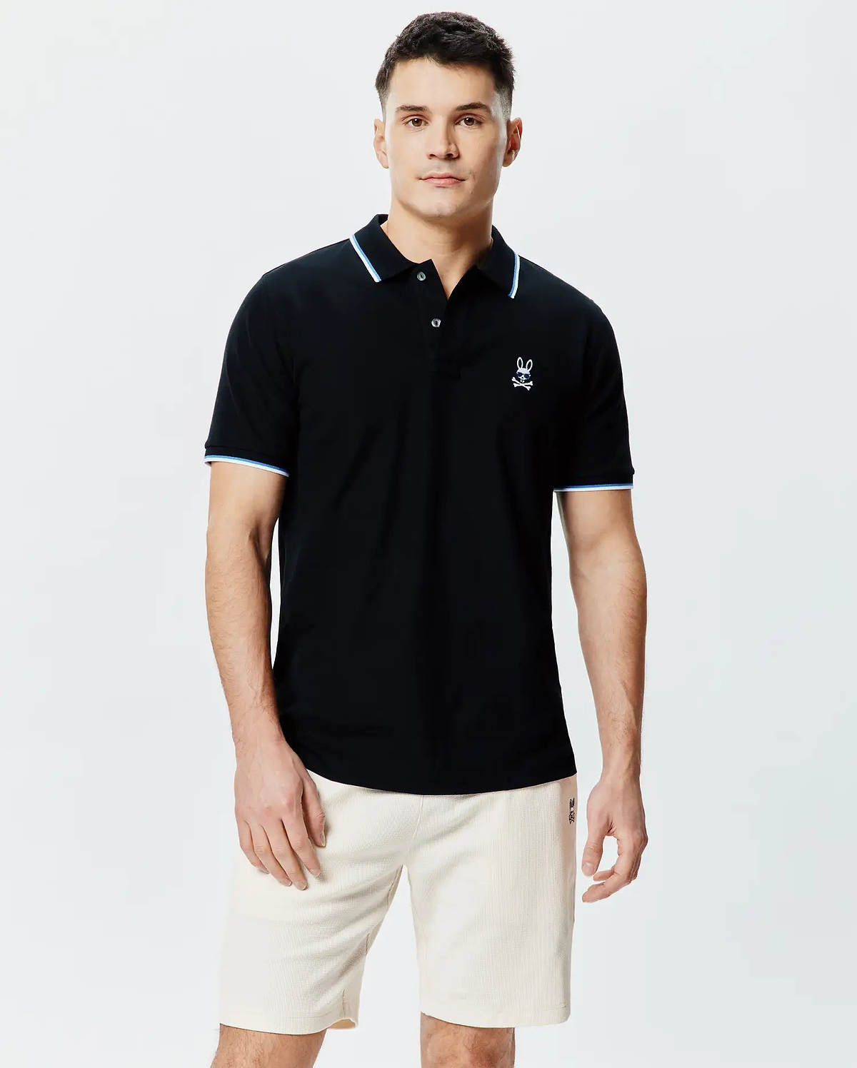 Mens Sunny Pique Polo, a classic fit black pique polo shirt with light blue and white striped collar and sleeve cuffs, featuring a small embroidered Psycho Bunny skull logo on the left chest. (1)