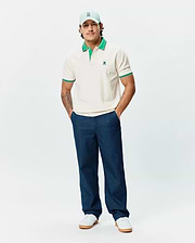 Mens Sunny Pique Polo, a classic fit cream pique polo shirt with a contrasting green collar, green and white striped cuffs, and a small embroidered green Psycho Bunny skull logo on the left chest.