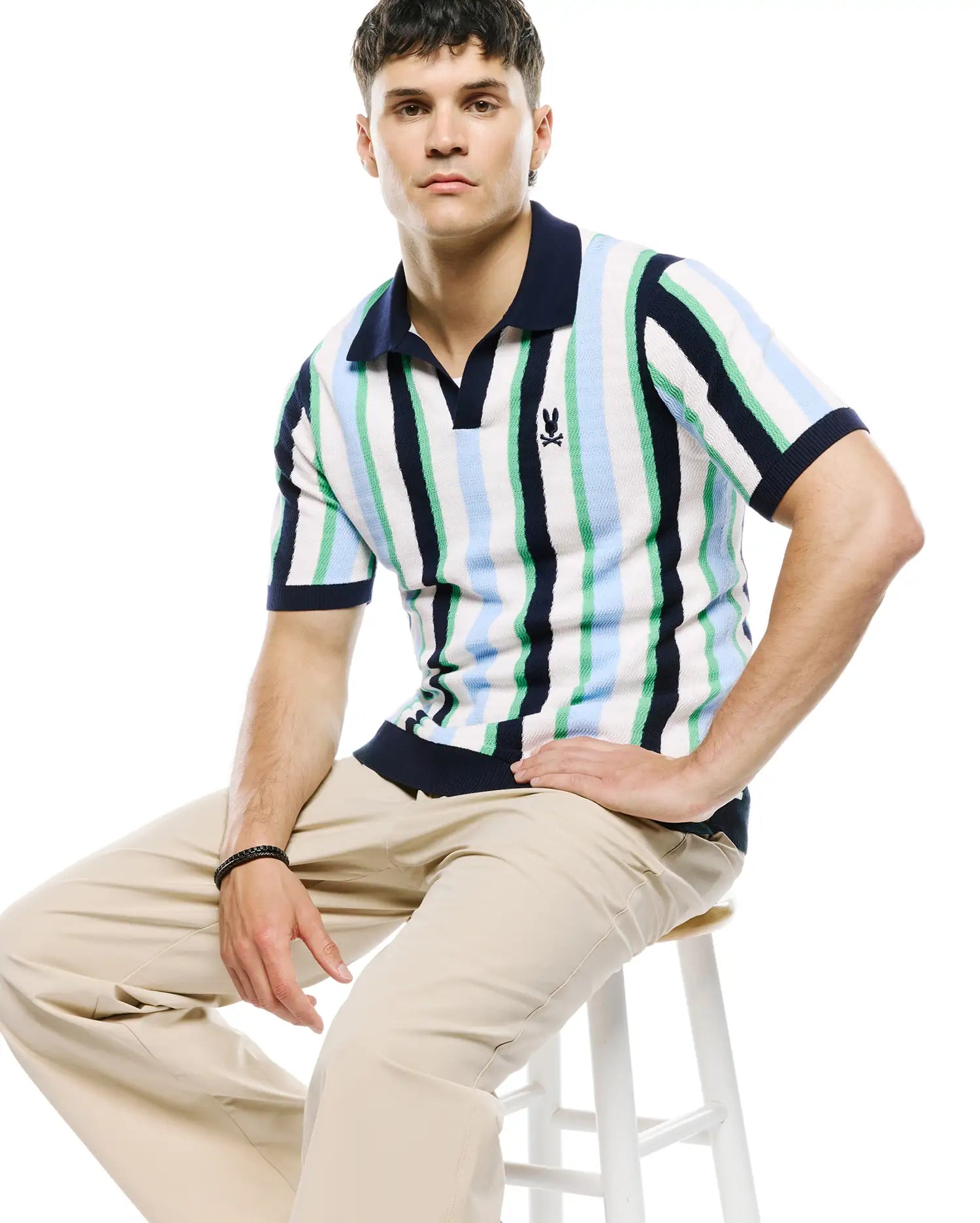 Mens Wren Stripe Knit Polo, a classic fit knit polo with bold vertical stripes in white, navy, light blue, and green, featuring a navy collar, V-neck placket, and small embroidered Psycho Bunny skull logo on the left chest. (2)