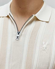 Mens Cliff Knit Zip Polo in cream with vertical beige stripes, featuring a ribbed knit texture, full collar, quarter-zip with custom Psycho Bunny zipper pull, and an embroidered cream bunny skull logo on the left chest.