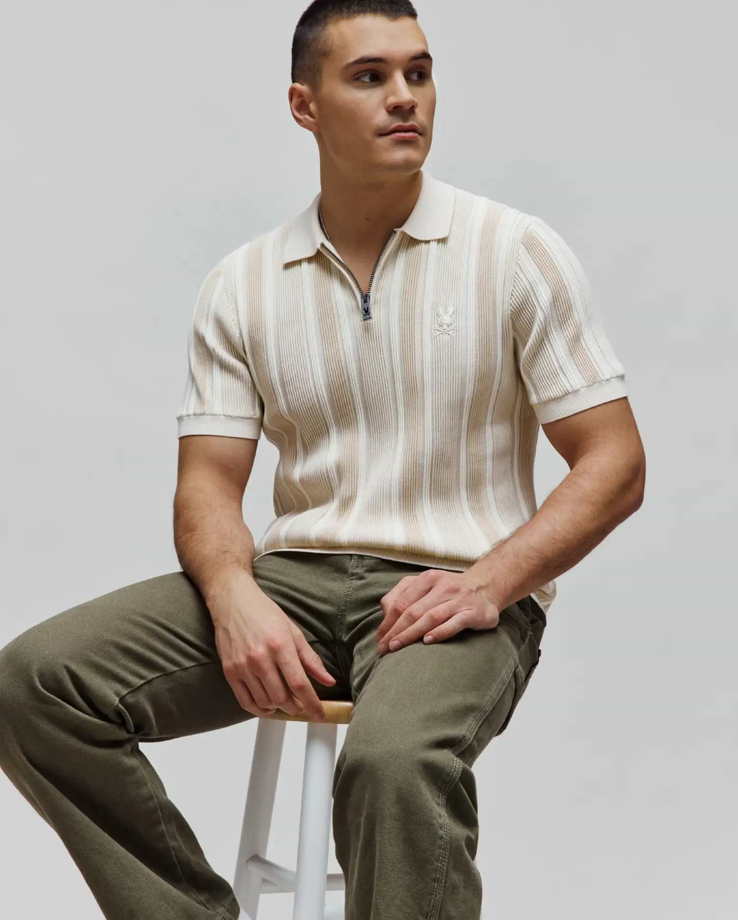 Mens Cliff Knit Zip Polo in cream and beige vertical stripes, featuring a ribbed knit texture, a quarter-zip closure with a Psycho Bunny logo pull, and a small embroidered cream bunny skull logo on the left chest for a slim fit.