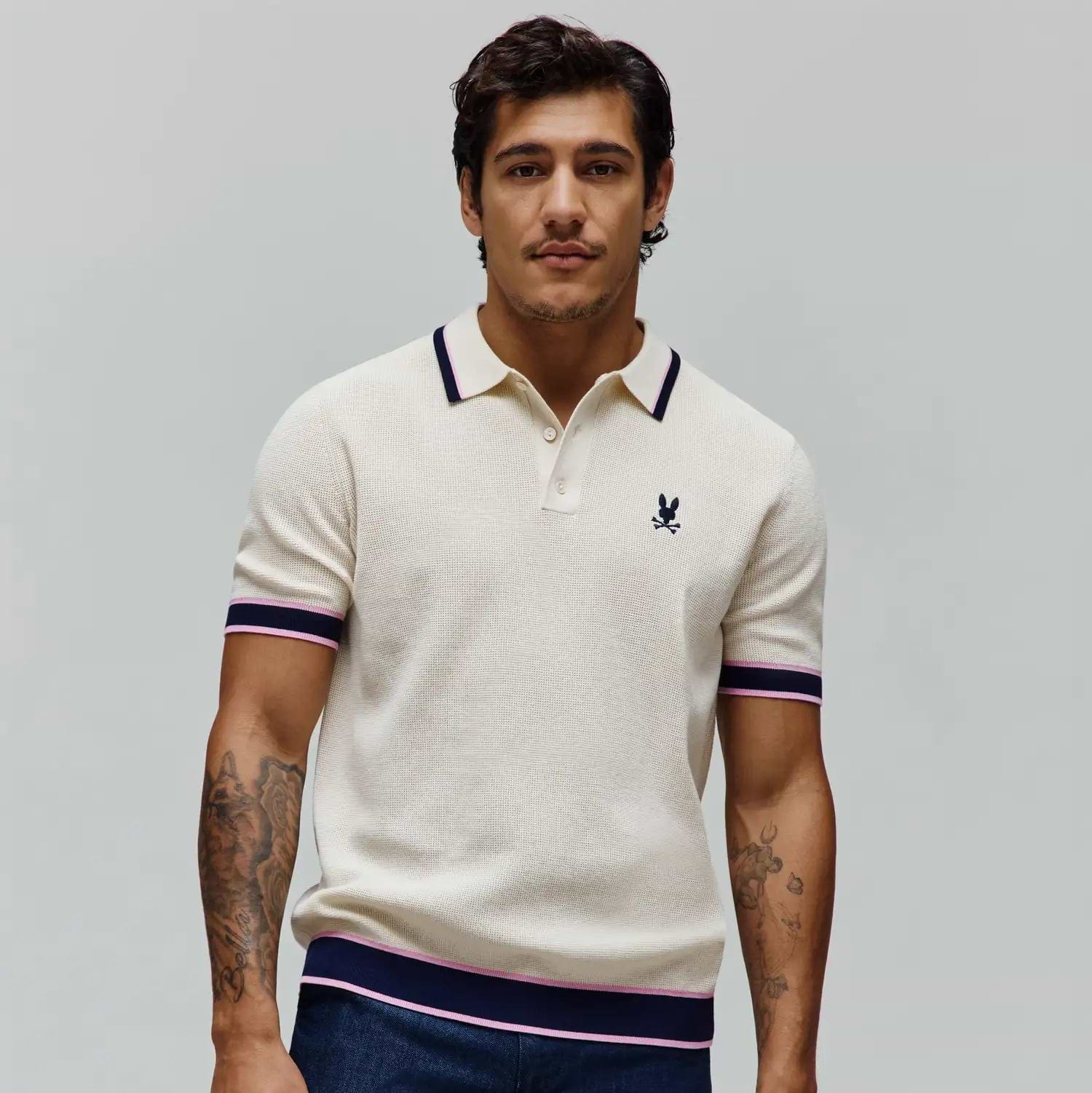 Mens Dax Knit Polo, cream textured knit with navy and pink striped collar, cuffs, and hem, featuring a small embroidered navy Psycho Bunny skull logo on the left chest. (2)