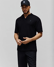 Mens Garen Knit Polo. Black, relaxed fit, textured knit polo with an open collar and a small, embroidered dark grey Psycho Bunny skull logo on the left chest. (1)
