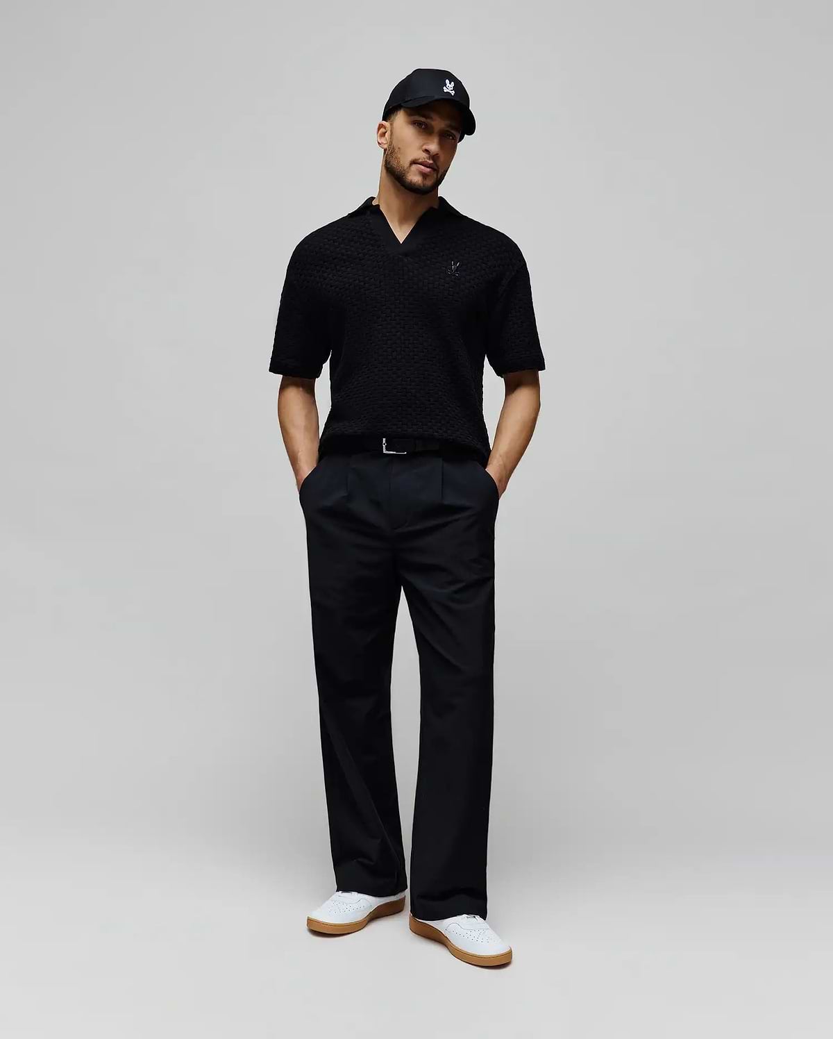 Mens Garen Knit Polo in black, featuring a textured knit fabric, open collar, and a small dark blue embroidered Psycho Bunny skull logo on the left chest for a classic fit. (3)