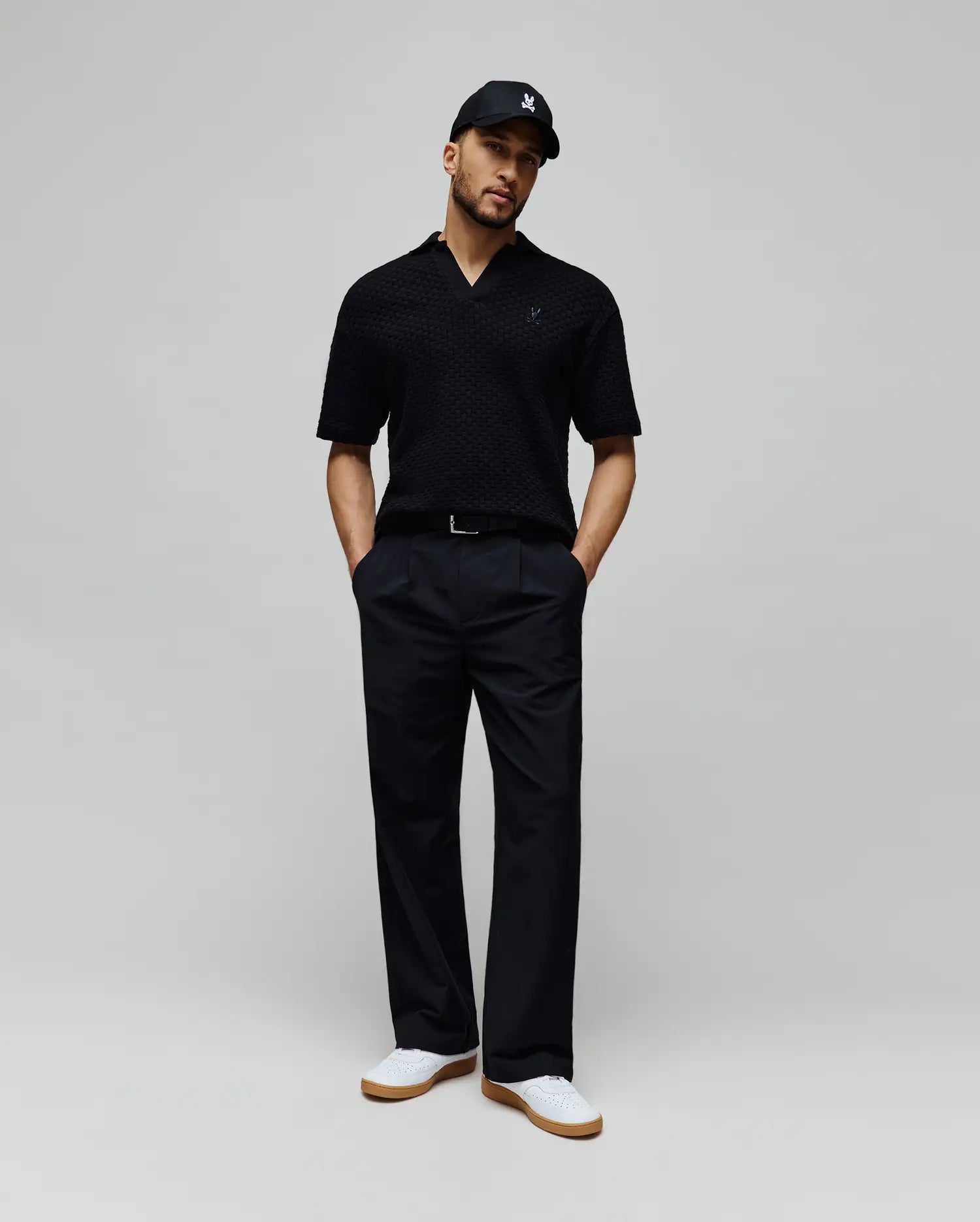 Mens Garen Knit Polo in black, featuring a textured knit fabric, open collar, and a small dark blue embroidered Psycho Bunny skull logo on the left chest for a classic fit. (3)