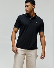 Mens Kenyon Pique Polo, black, classic fit, with white striped collar and sleeve cuffs, featuring a pique texture and a small white embroidered Psycho Bunny skull logo on the left chest. (1)