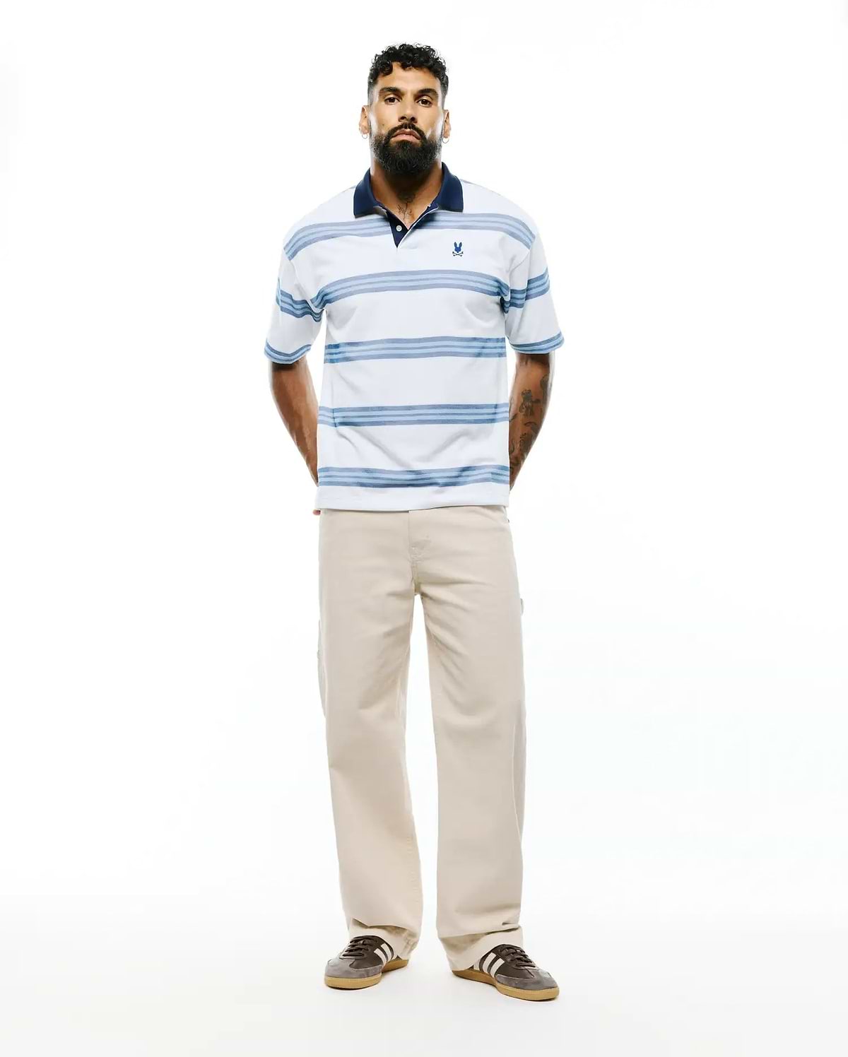 Mens Drew Striped Pique Polo, a classic fit white pique polo with navy collar, light blue horizontal stripes, and a small embroidered Psycho Bunny skull logo on the left chest. (3)
