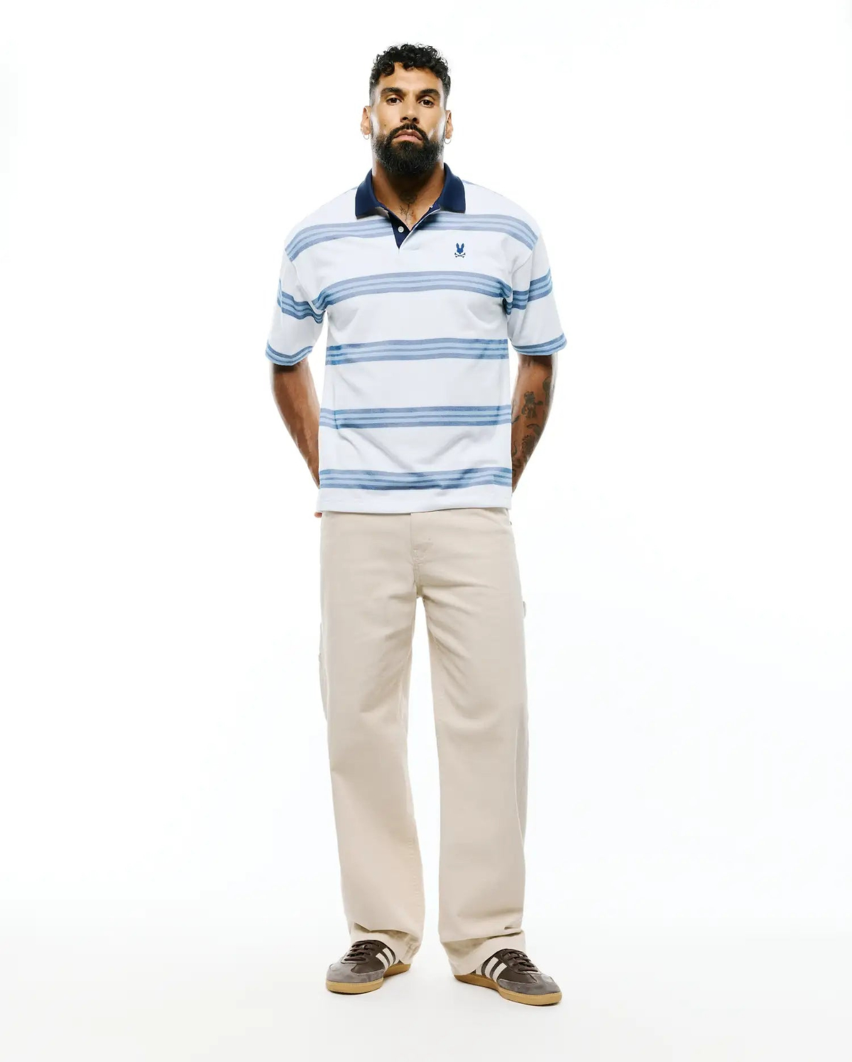Mens Drew Striped Pique Polo, a classic fit white pique polo with navy collar, light blue horizontal stripes, and a small embroidered Psycho Bunny skull logo on the left chest. (3)