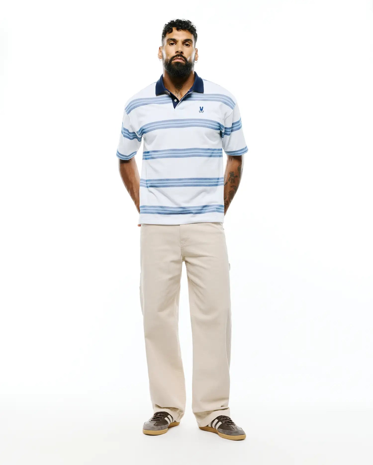 Mens Drew Striped Pique Polo, a classic fit white pique polo with navy collar, light blue horizontal stripes, and a small embroidered Psycho Bunny skull logo on the left chest. (3)