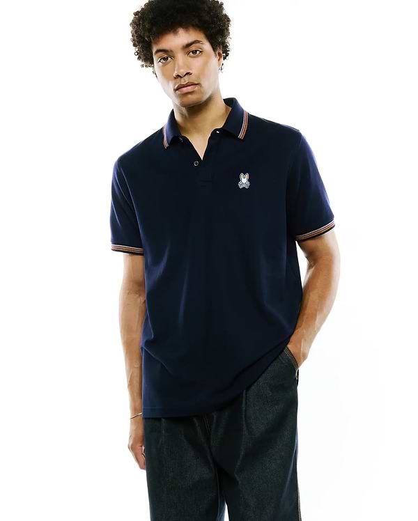 Mens Jaydon Pique Polo, navy classic fit pique knit with a small embroidered Psycho Bunny skull logo on the left chest and striped collar and sleeve cuffs in orange, white, and blue. (1)
