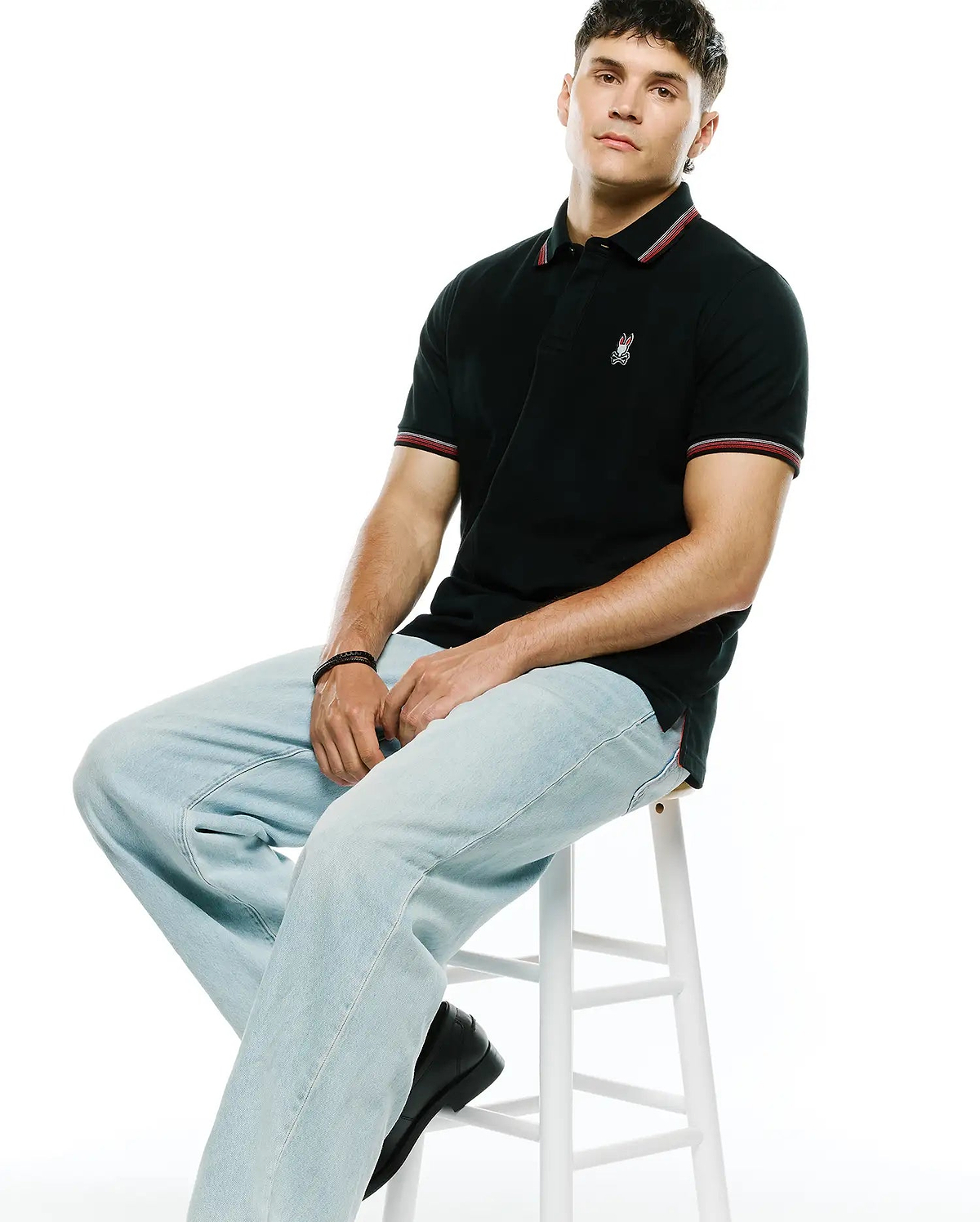 Mens Jaydon Pique Polo in black, featuring a classic fit, textured pique fabric, red and white striped collar and cuffs, and a small embroidered Psycho Bunny skull logo on the left chest. (3)