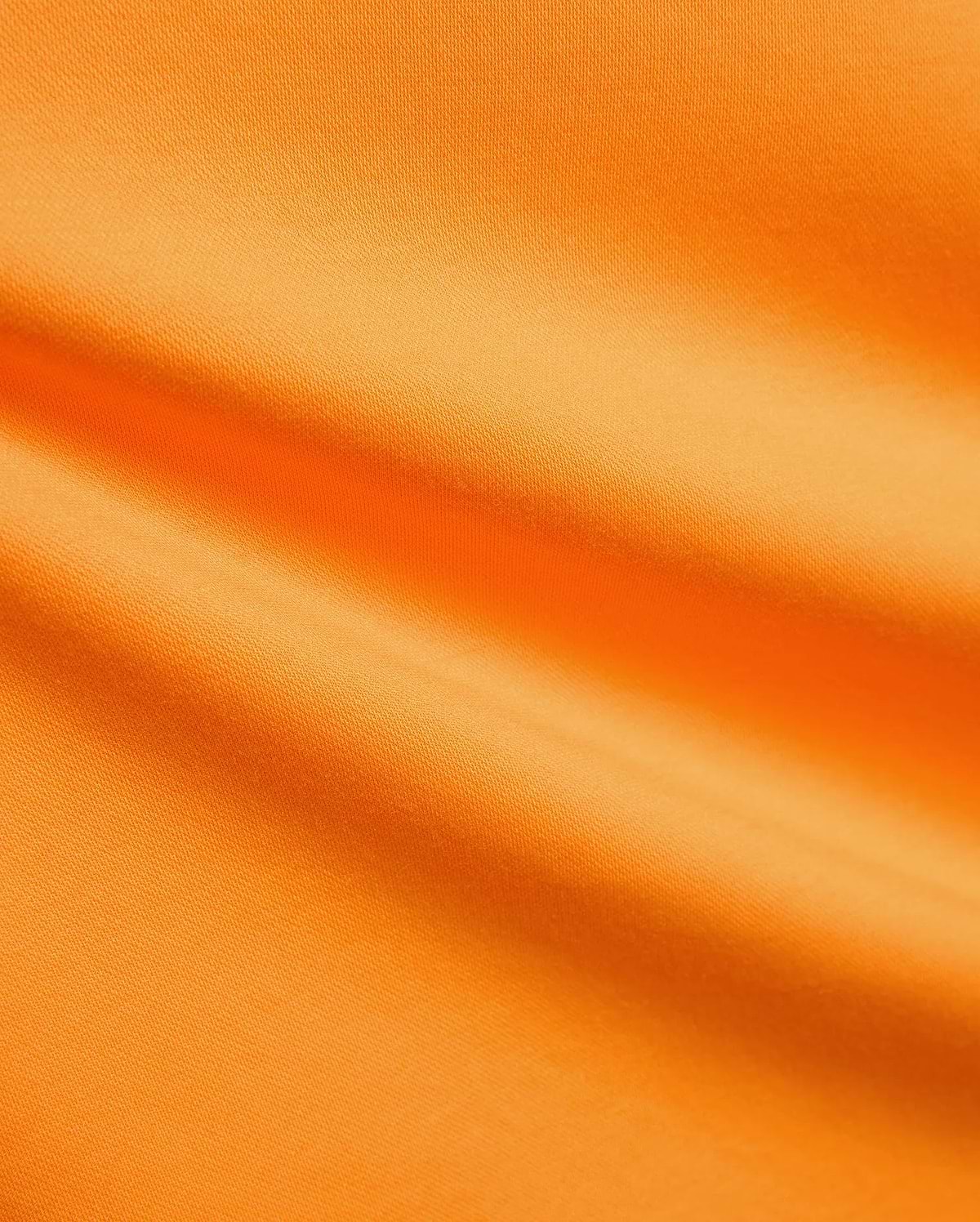 Mens Joji Performance Polo in a bright, energetic orange, featuring a finely textured, breathable pique knit fabric with subtle diagonal lines and soft folds, ideal for refined streetwear. (5)
