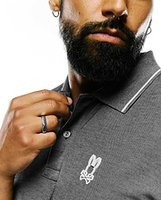 Mens Joji Performance Polo, a grey pique knit polo shirt featuring a classic fit, white tipping on the collar, a two-button placket, and a white embroidered Psycho Bunny skull logo on the left chest.