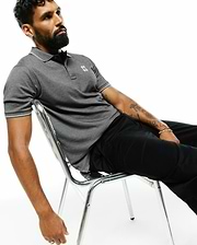 MENS JOJI PERFORMANCE POLO, a dark grey pique knit polo with a classic fit, white tipping on the collar and sleeve cuffs, and a small embroidered Psycho Bunny skull logo on the left chest.