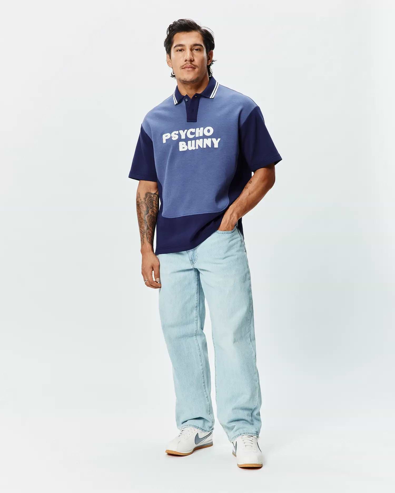 Mens Kelly Oversized Polo, a two-tone blue color block jersey polo with an oversized fit, featuring white collar stripes and a large white PSYCHO BUNNY text logo across the chest. (4)