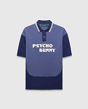 Mens Kelly Oversized Polo, an oversized two-tone blue jersey polo with medium blue and navy color-block, white-striped navy collar, large white embroidered PSYCHO BUNNY chest text, and small back neck bunny skull logo. (5)