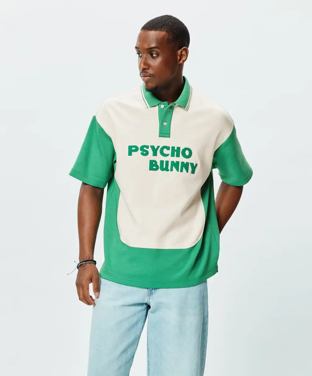 Mens Kelly Oversized Polo, a kelly green and cream color block polo with an oversized fit. Features a soft jersey texture, short sleeves, and large embroidered PSYCHO BUNNY text on the cream chest.