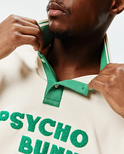 Mens Kelly Oversized Polo in cream jersey, featuring a vibrant green ribbed collar with white stripes, white buttons, and a large, textured green chenille PSYCHO BUNNY appliqué on the chest.