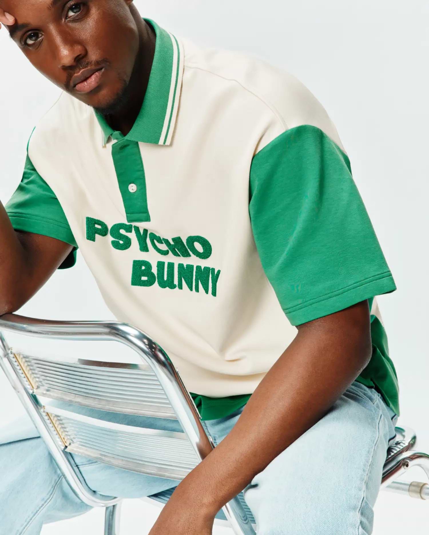 Mens Kelly Oversized Polo, a cream and green color block jersey polo with an oversized fit, featuring a large embroidered Psycho Bunny text logo on the chest and a small bunny skull on the sleeve.