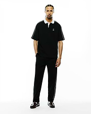 Mens Ceano Relaxed Fit Heavy Pique Polo, black with a crisp white collar, white cuffs, and white piping detail along the shoulders and sleeves, featuring a small embroidered white Psycho Bunny skull logo on the left chest.