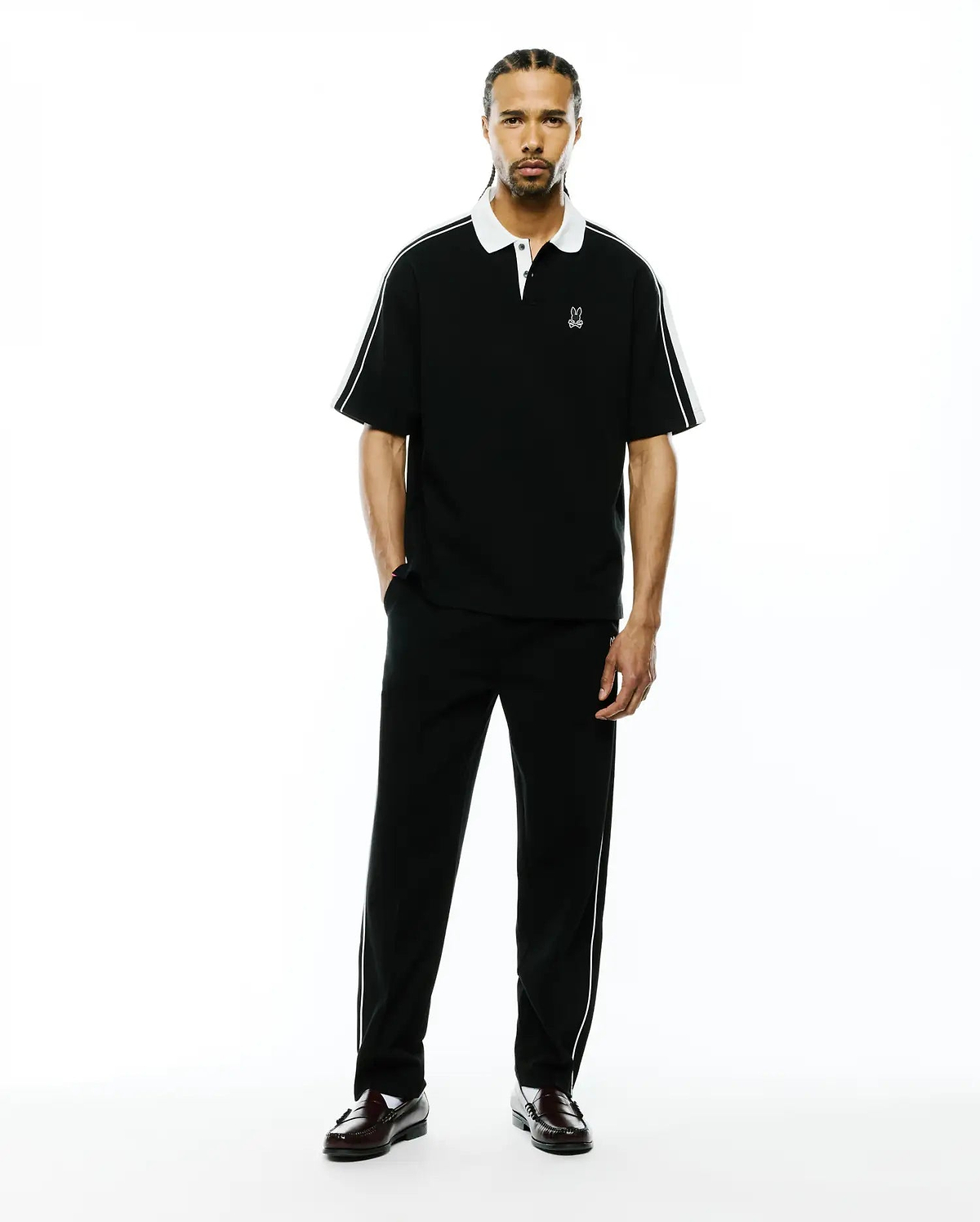 Mens Ceano Relaxed Fit Heavy Pique Polo, black with a crisp white collar, white cuffs, and white piping detail along the shoulders and sleeves, featuring a small embroidered white Psycho Bunny skull logo on the left chest.