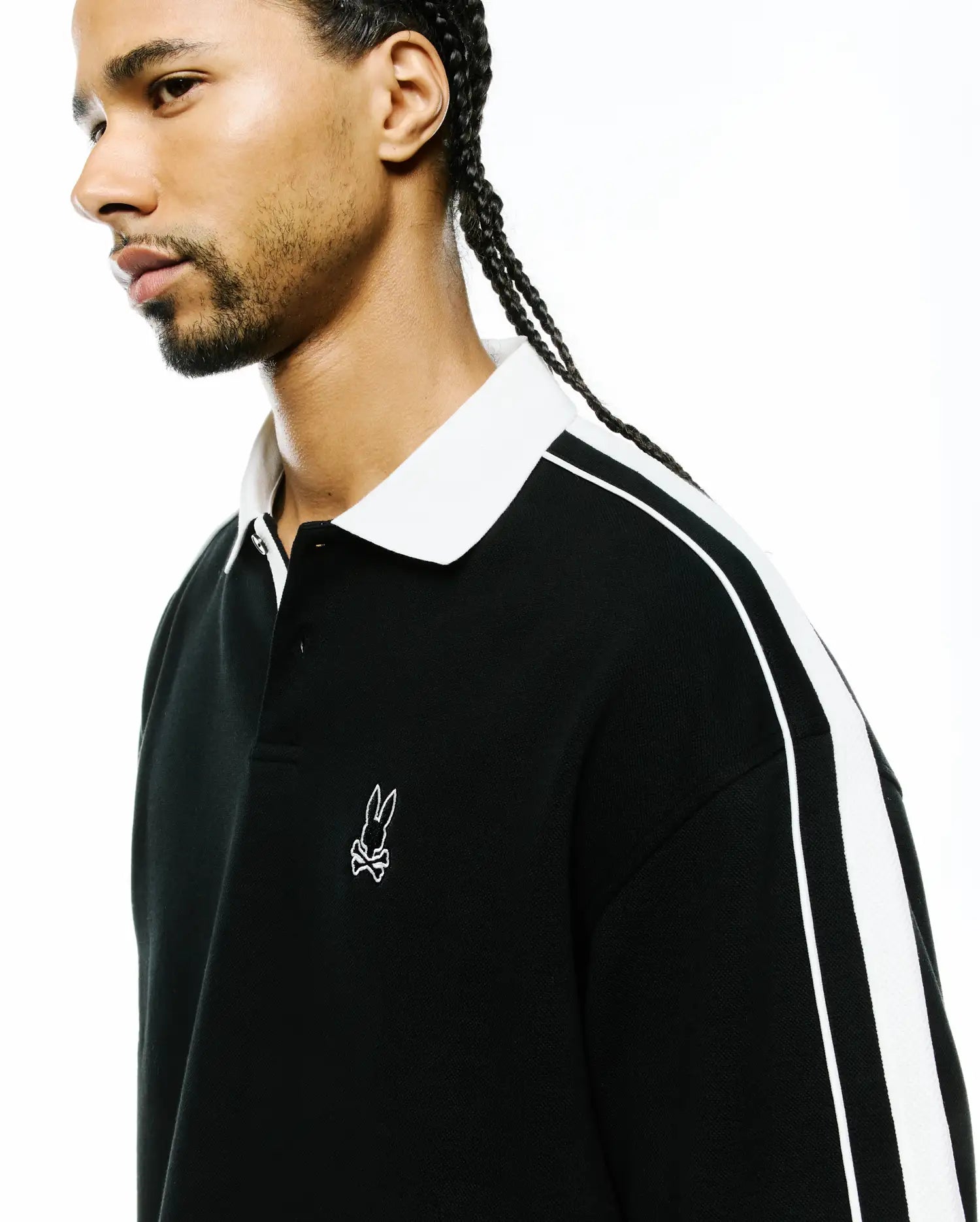 Mens Ceano Relaxed Fit Heavy Pique Polo in black with a crisp white collar, bold white double stripes on the sleeves, and a small white embroidered Psycho Bunny skull logo on the left chest.