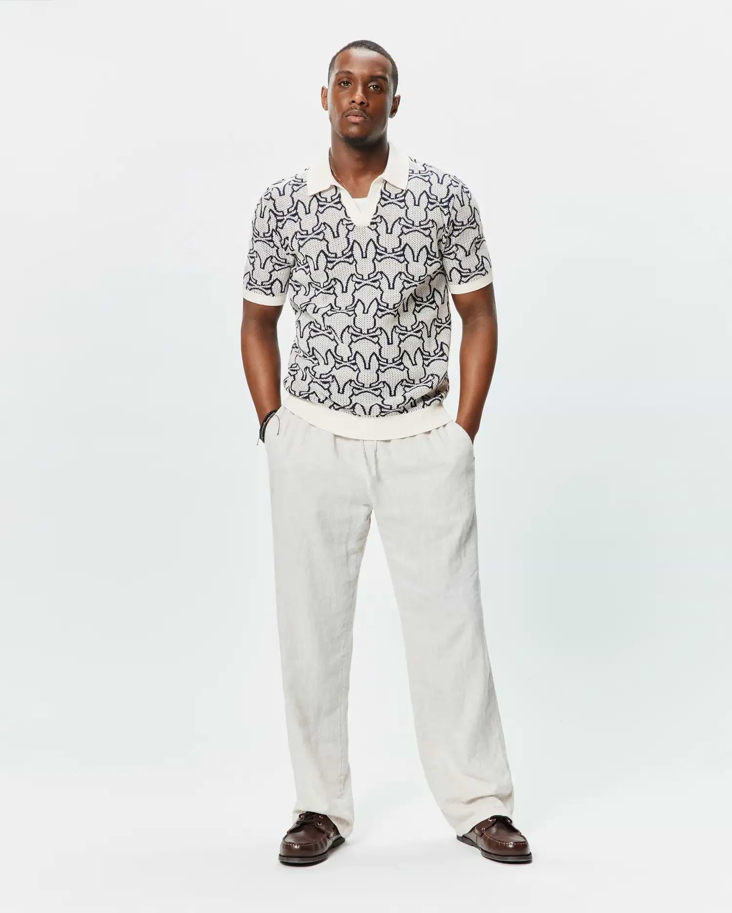 Mens Sidney Oversized Knit Polo in cream, featuring a relaxed fit and a textured knit fabric with an all-over dark blue Psycho Bunny skull logo pattern, complete with ribbed collar, cuffs, and hem. (1)