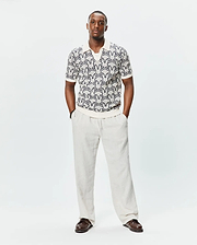 Mens Sidney Oversized Knit Polo in cream, featuring a relaxed fit and a textured knit fabric with an all-over dark blue Psycho Bunny skull logo pattern, complete with ribbed collar, cuffs, and hem. (1)