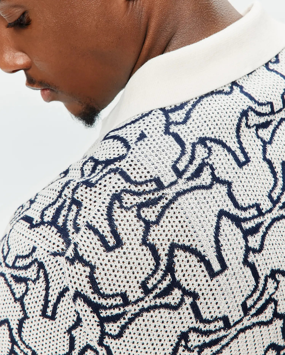 Mens Sidney Oversized Knit Polo in cream with an all-over navy blue abstract bunny skull pattern, featuring a textured open-knit fabric and a solid cream ribbed collar. (3)