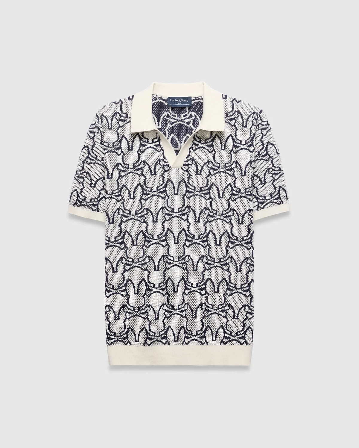 Mens Sidney Oversized Knit Polo, a cream and navy blue jacquard knit polo featuring an all-over Psycho Bunny skull logo pattern, solid cream collar, cuffs, and an oversized fit. (4)