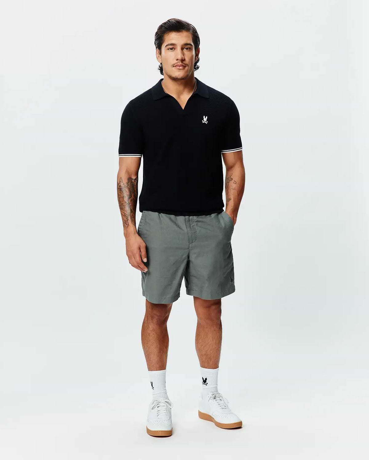 Black MENS SELBY KNIT POLO, classic fit, with an open collar, fine knit texture, white double-striped sleeve cuffs, and a small embroidered white Psycho Bunny skull logo on the left chest. (3)