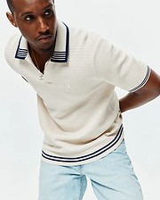 Mens Elowen Knit Polo in cream, featuring a ribbed knit texture, navy and white striped collar, cuffs, and hem, with a small embroidered Psycho Bunny skull logo on the left chest. (1)