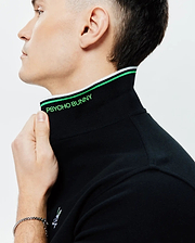 Mens Faye Pique Polo, black with a classic fit, features a ribbed collar accented with green and white stripes, bright green PSYCHO BUNNY text on the inner collar, and a small embroidered bunny skull logo. (2)
