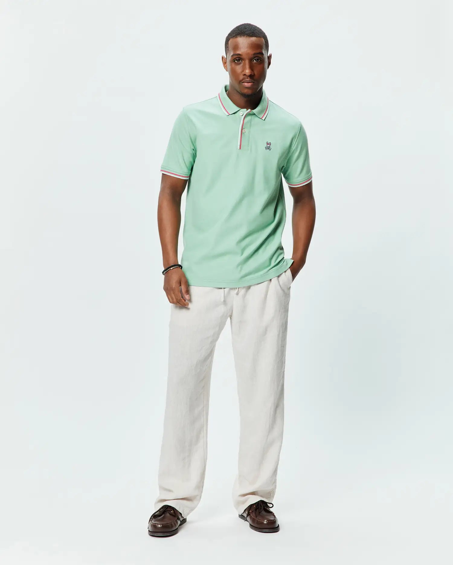 Mens Faye Pique Polo in mint green, a classic fit pique knit with ribbed collar and cuffs featuring red and white tipping, and a small embroidered Psycho Bunny skull logo on the left chest.
