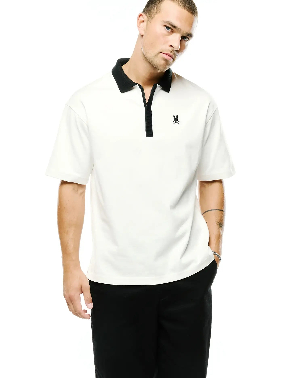 Men's Nolen Oversized Jersey Polo in creamy white, featuring a black ribbed collar, black zippered placket, and a small embroidered Psycho Bunny skull logo on the left chest. (1)