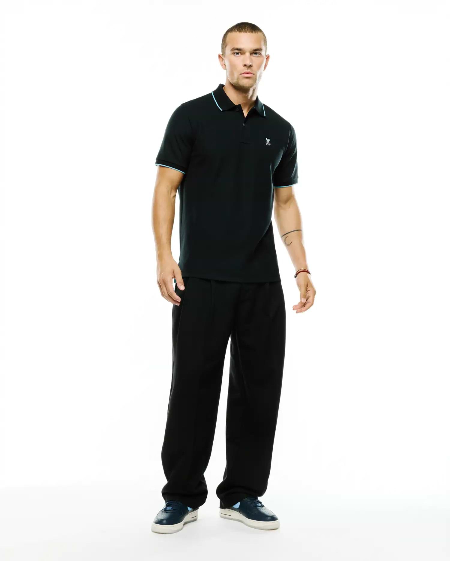 Men's Klaus Pique Polo, a classic fit black pique polo with light blue tipping on the collar and sleeve cuffs, featuring a small embroidered Psycho Bunny skull logo on the left chest. (4)